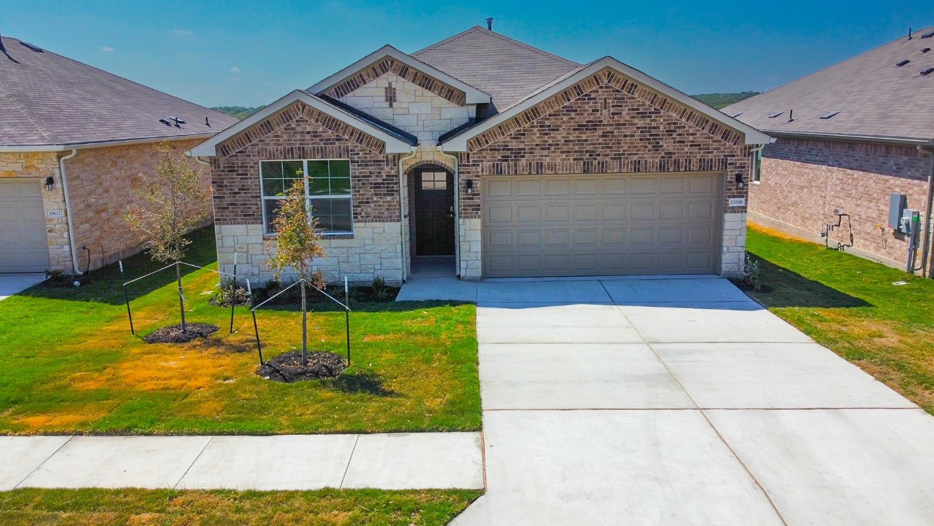 10616 Defender Trail Austin, TX 78754 - Photo 1 of 25 View of front facade featuring stone siding, a garage, driveway, brick siding, and a front yard