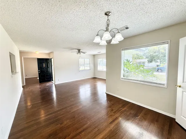 an empty room with wooden floor chandelier and windows