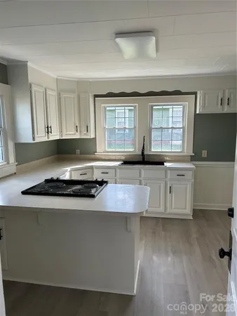 a large kitchen with granite countertop a stove a sink a refrigerator and white cabinets with wooden floor