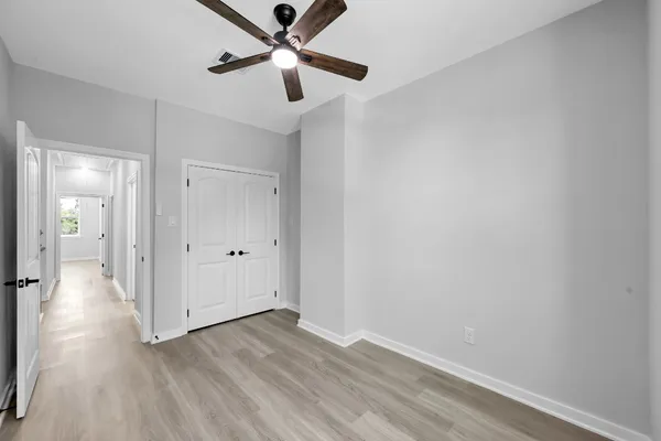an empty room with wooden floor a ceiling fan and kitchen view