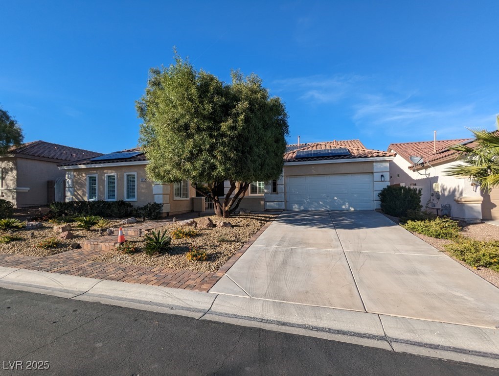 View of front of house featuring driveway, roof mounted solar panels, stucco siding, an attached garage, and a tile roof