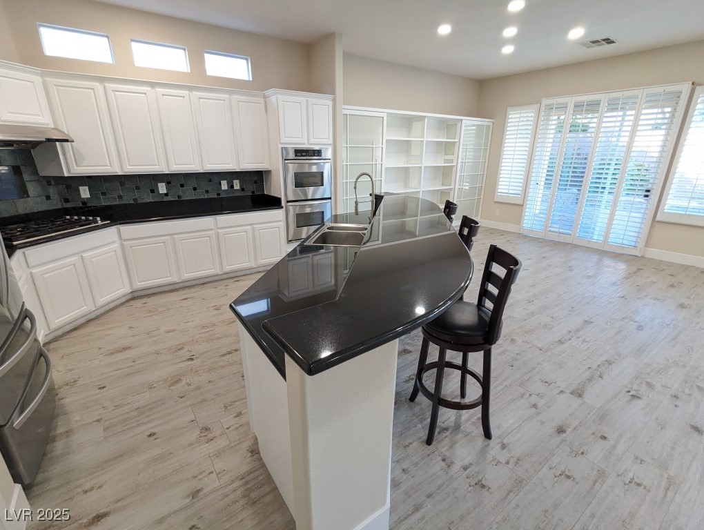 9976 Liberty View Road Las Vegas, NV 89148 - Photo 8 of 44 Kitchen featuring white cabinetry, a breakfast bar area, an island with sink, tasteful backsplash, and stainless steel appliances