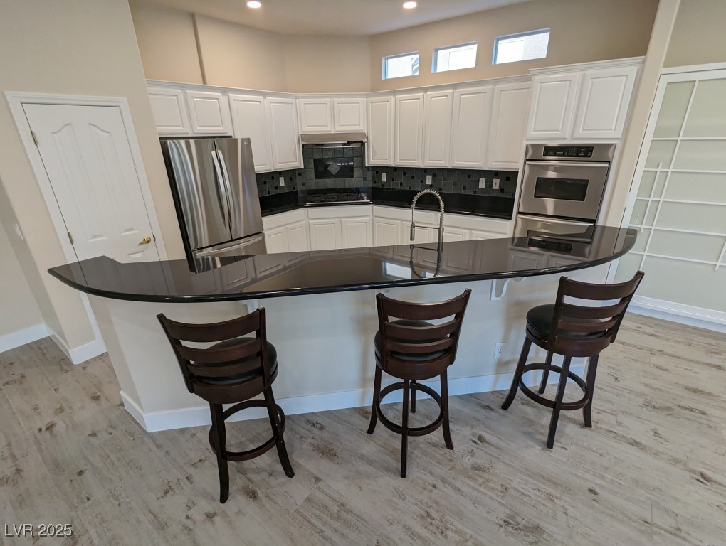 9976 Liberty View Road Las Vegas, NV 89148 - Photo 9 of 44 Kitchen with white cabinets, appliances with stainless steel finishes, a breakfast bar area, a spacious island, and backsplash