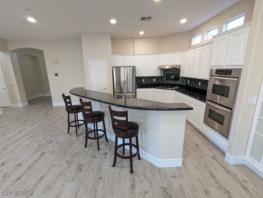 9976 Liberty View Road Las Vegas, NV 89148 - Photo 7 of 44 Kitchen with white cabinetry, arched walkways, a breakfast bar, appliances with stainless steel finishes, and a spacious island
