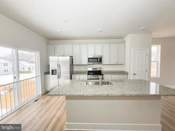 a large living room with stainless steel appliances granite countertop a stove a sink a refrigerator and white cabinets with wooden floor