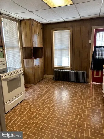 a view of a refrigerator in kitchen and an empty room with wooden floor