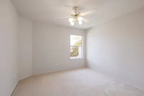 an empty room with a chandelier fan and windows