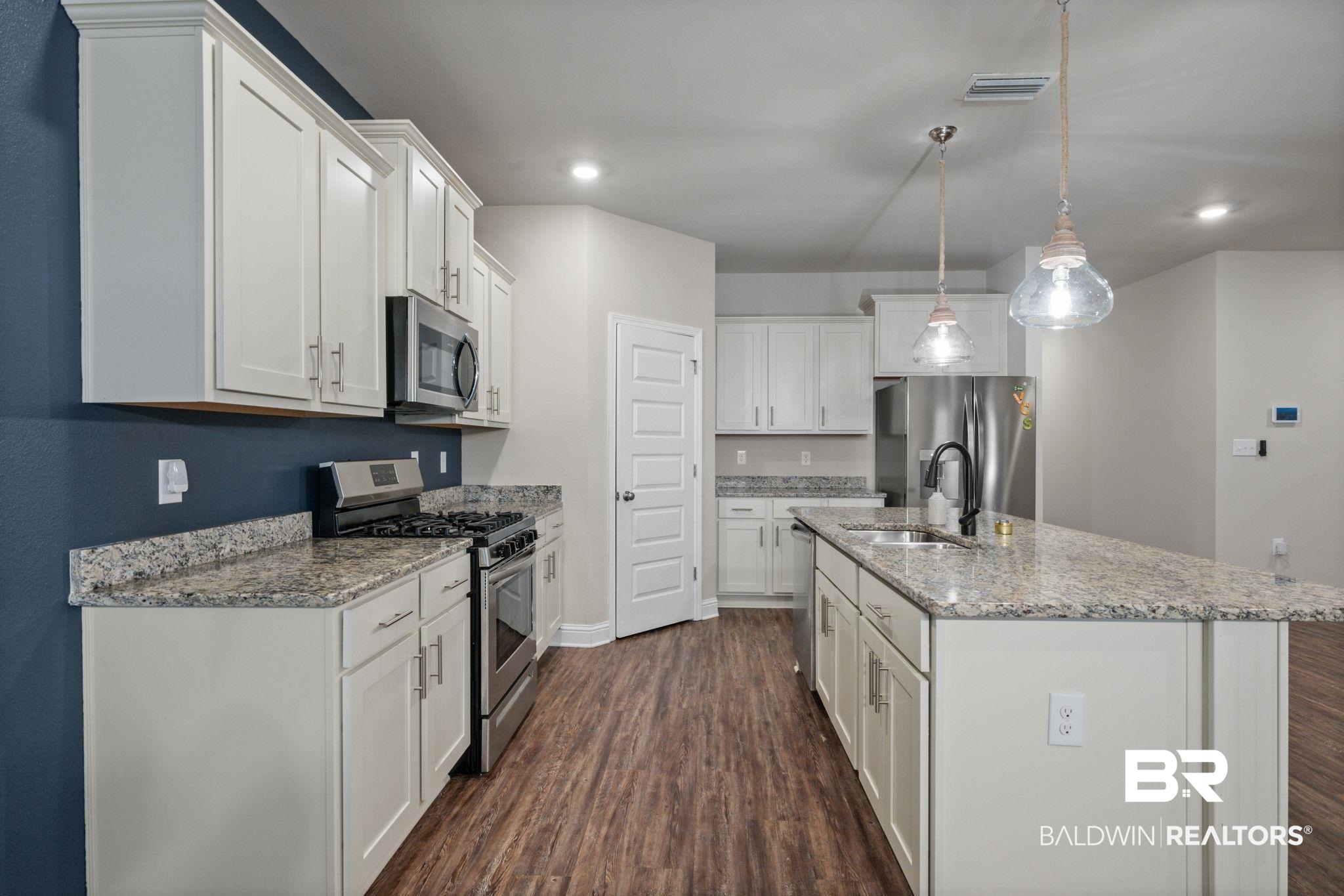 24769 Slater Mill Road Daphne, AL 36526 - Photo 11 of 38 Kitchen featuring dark hardwood / wood-style flooring, a kitchen island with sink, appliances with stainless steel finishes, white cabinets, and light stone counters