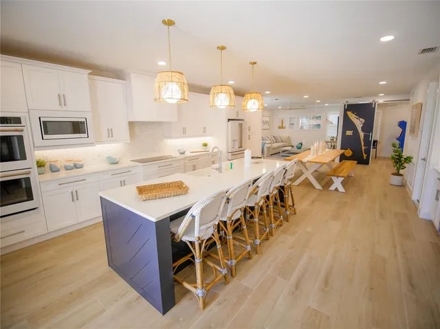 a large kitchen with kitchen island a large counter top a chandelier and stainless steel appliances
