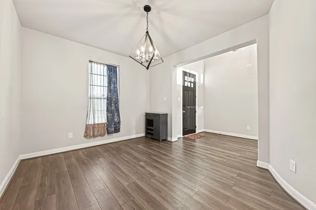 an empty room with wooden floor chandelier and windows