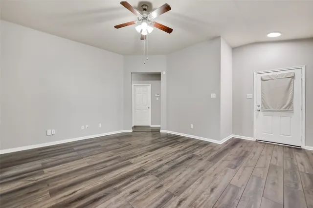 a view of an empty room with wooden floor and a ceiling fan