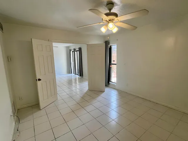 an empty room with fan and way to kitchen