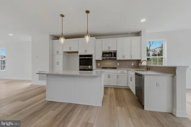 a kitchen with stainless steel appliances granite countertop a stove a sink and white cabinets with wooden floor