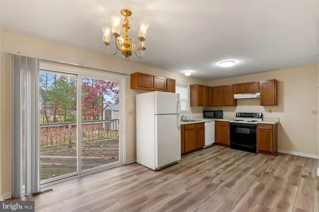 a kitchen with kitchen island granite countertop a refrigerator oven a sink dishwasher and white cabinets with wooden floor