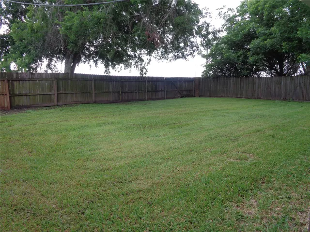 a view of a backyard with large trees and wooden fence
