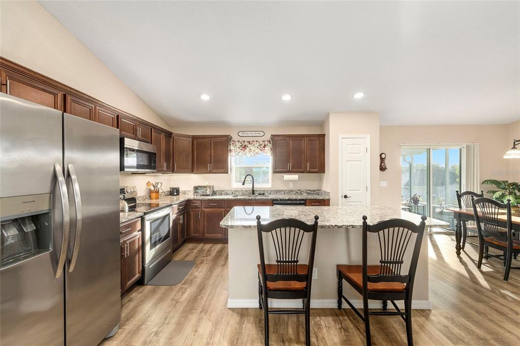 13057 Southwest 85th Circle Ocala, FL 34473 - Photo 3 of 34 a kitchen with stainless steel appliances granite countertop a stove top oven a sink dishwasher a dining table and chairs with wooden floor