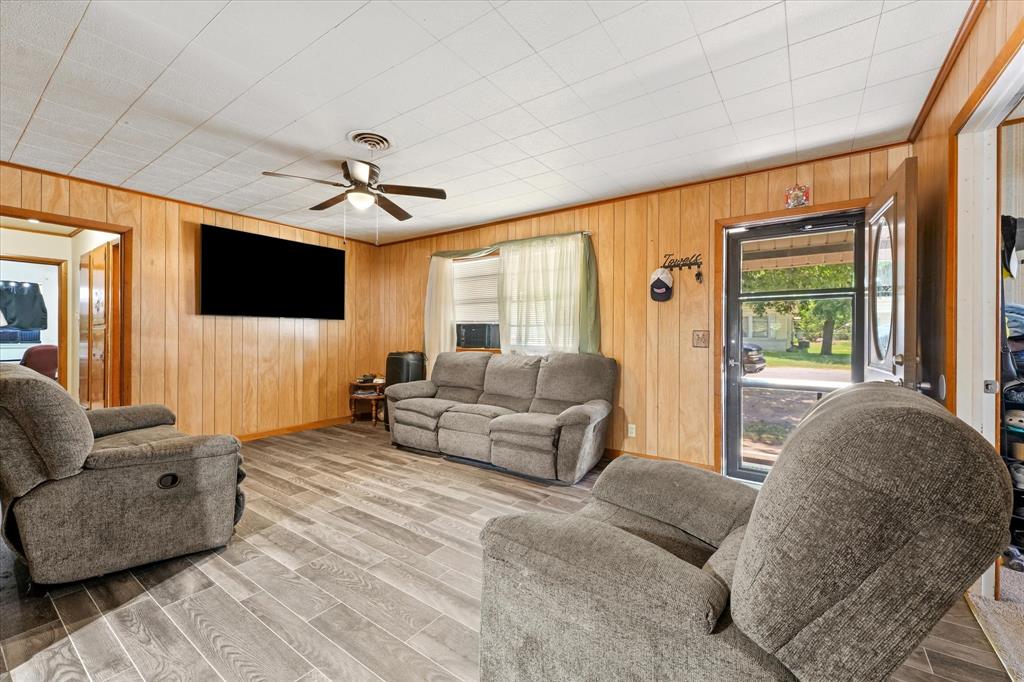 1100 North Church Street Decatur, TX 76234 - Photo 5 of 14 Living area featuring wood-finish paneling, a ceiling fan with integrated lighting, wood-finish flooring, and a front entry door with a storm door