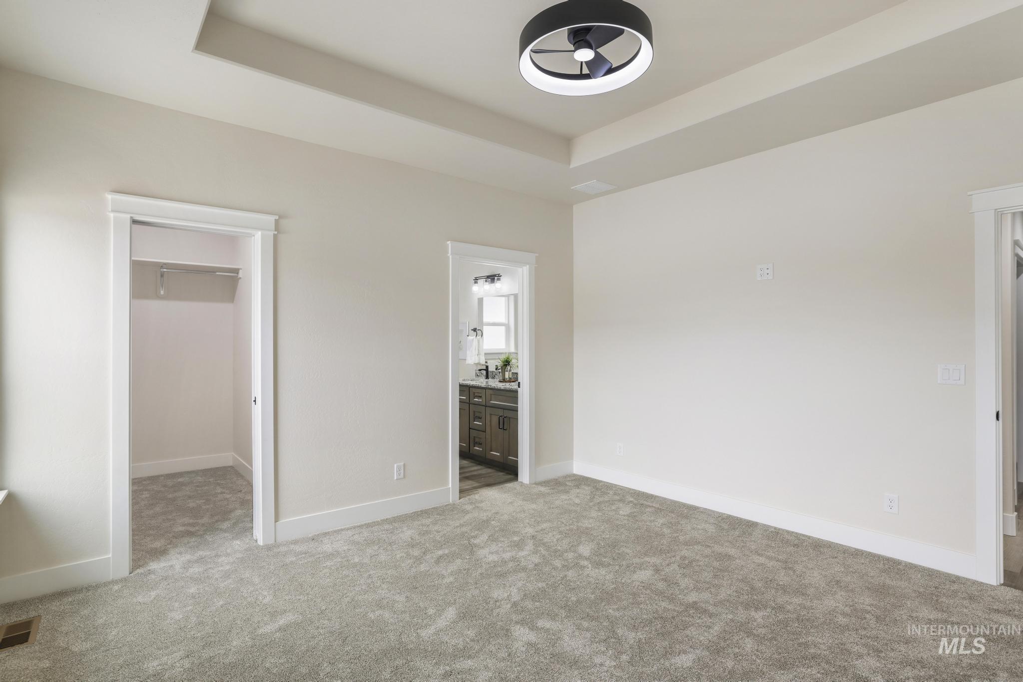 928 Gregory Way Twin Falls, ID 83301 - Photo 13 of 24 Unfurnished bedroom featuring a raised ceiling, a spacious closet, light carpet, and connected bathroom