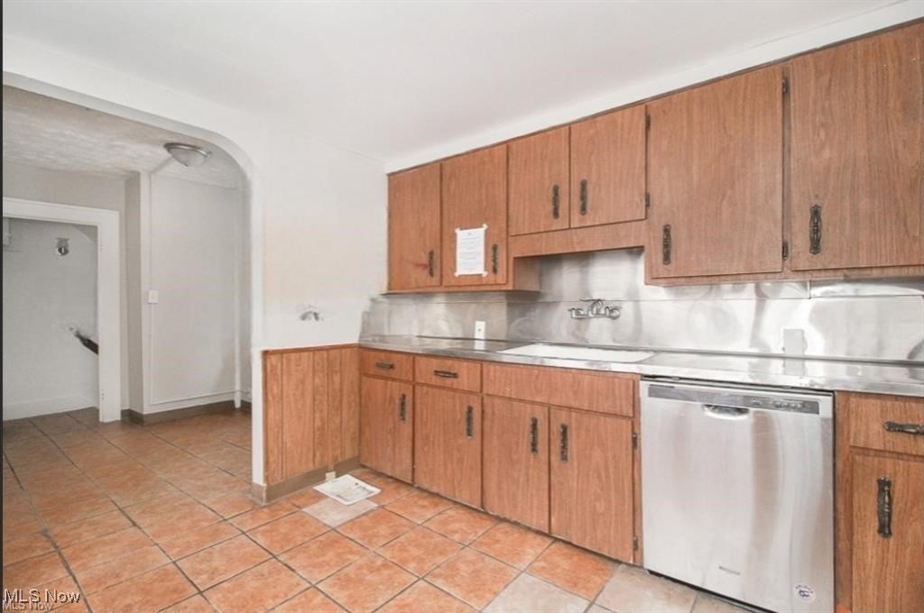 Kitchen featuring light tile patterned flooring, a sink, dishwasher, brown cabinetry, and decorative backsplash