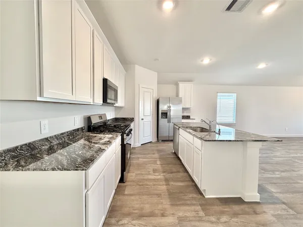 a large kitchen with stainless steel appliances granite countertop a stove top oven a sink dishwasher and a refrigerator