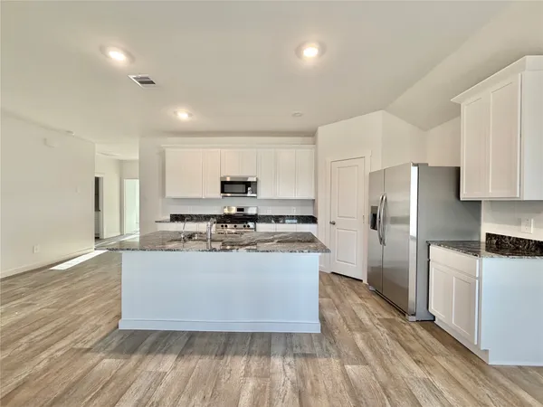 a kitchen with stainless steel appliances granite countertop a stove a refrigerator a sink a microwave and white cabinets with wooden floor