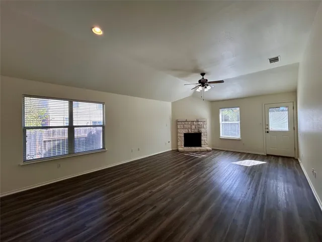 an empty room with wooden floor fireplace and windows