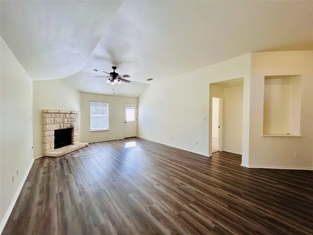 a view of an empty room with wooden floor fireplace and a window