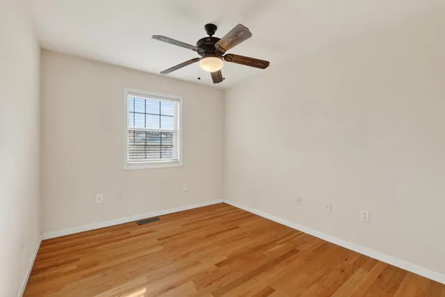 an empty room with wooden floor fan and windows