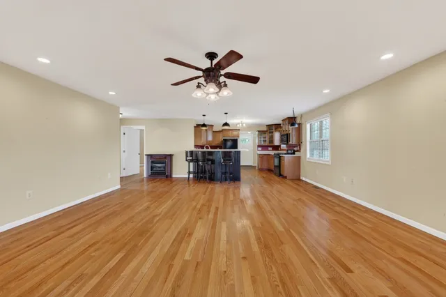 a view of a room with wooden floor a ceiling fan and kitchen space