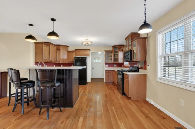 a kitchen with stainless steel appliances kitchen island granite countertop a stove a refrigerator a sink a dining table and chairs with wooden floor