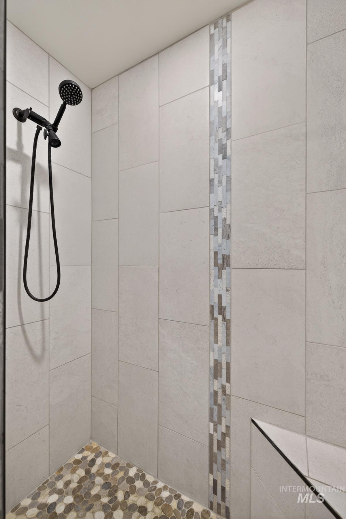 13388 Norwood Road McCall, ID 83638 - Photo 35 of 44 Shower enclosure featuring large format wall tiling, a vertical mosaic tile accent, pebble-finish floor tiling, a built-in shower bench, and matte black shower fixtures