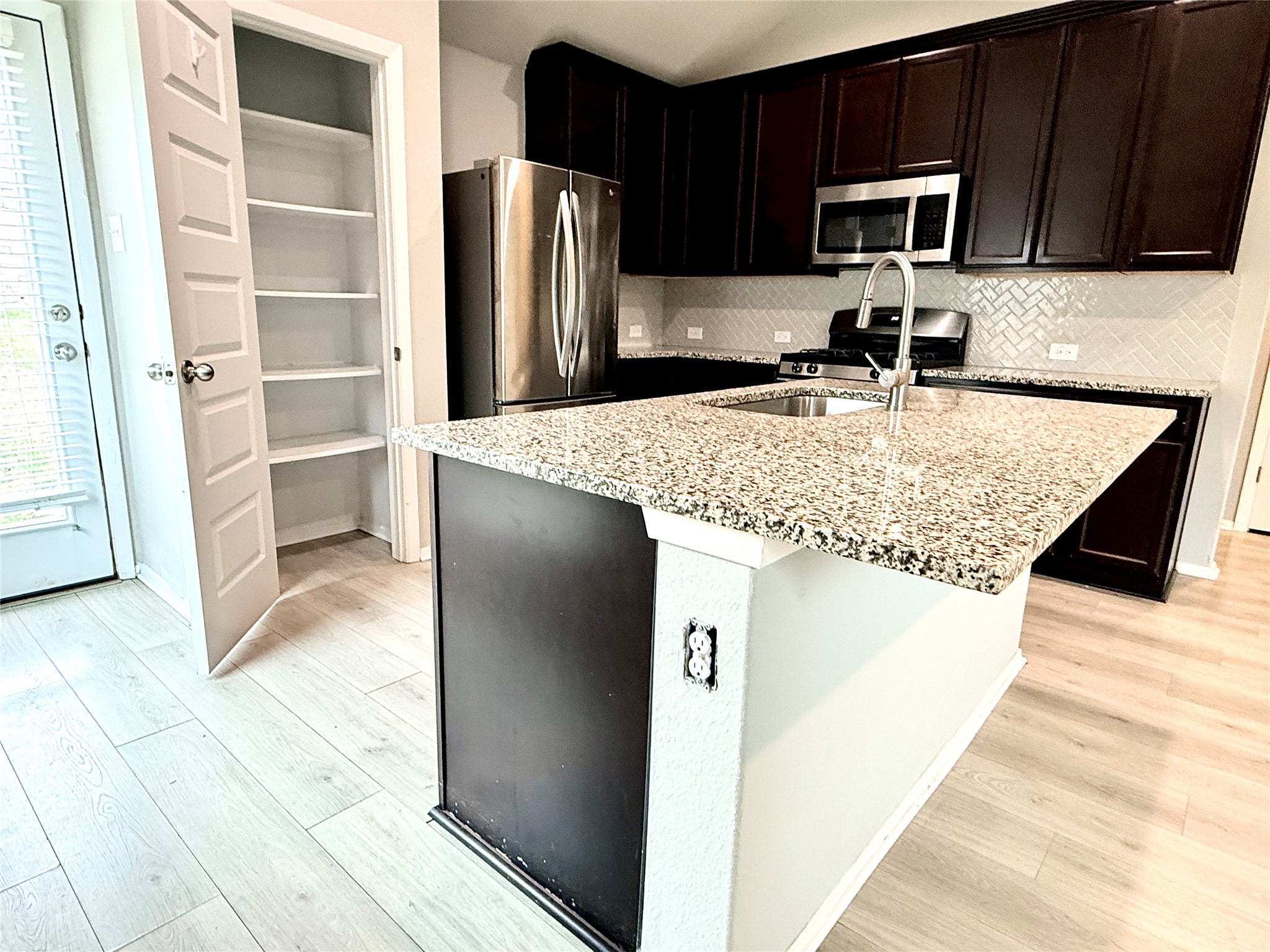 5629 Corso Court Austin, TX 78747 - Photo 11 of 23 Kitchen featuring stainless steel appliances, light stone counters, light wood-style floors, a kitchen island with sink, and dark wood finish cabinetry