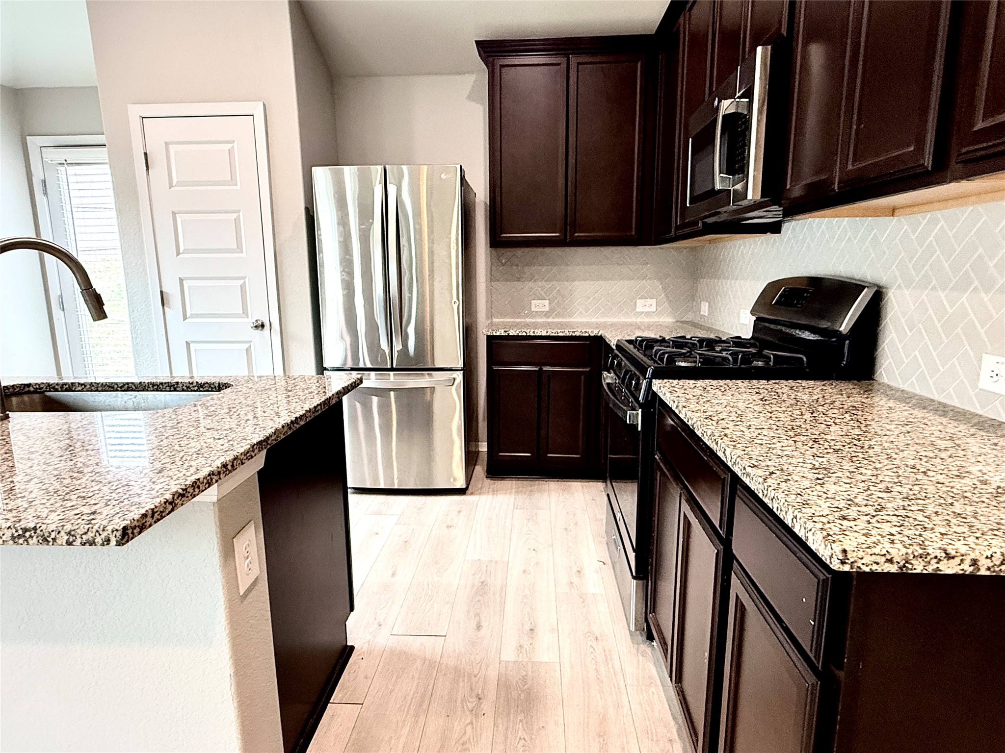 5629 Corso Court Austin, TX 78747 - Photo 4 of 23 Kitchen featuring stainless steel appliances, light stone countertops, dark wood finish cabinets, light wood-style floors, and backsplash