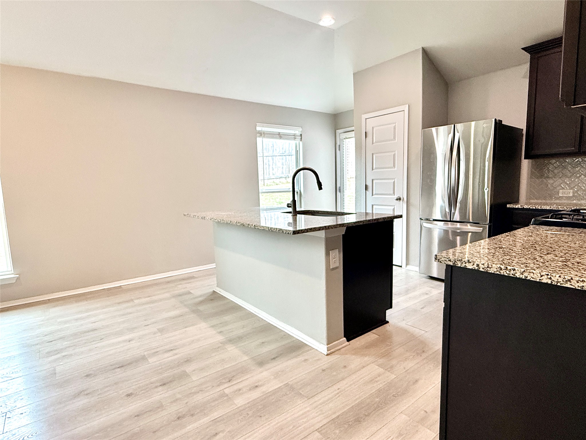 5629 Corso Court Austin, TX 78747 - Photo 6 of 23 Kitchen featuring freestanding refrigerator, light stone counters, tasteful backsplash, a center island with sink, and light wood-type flooring