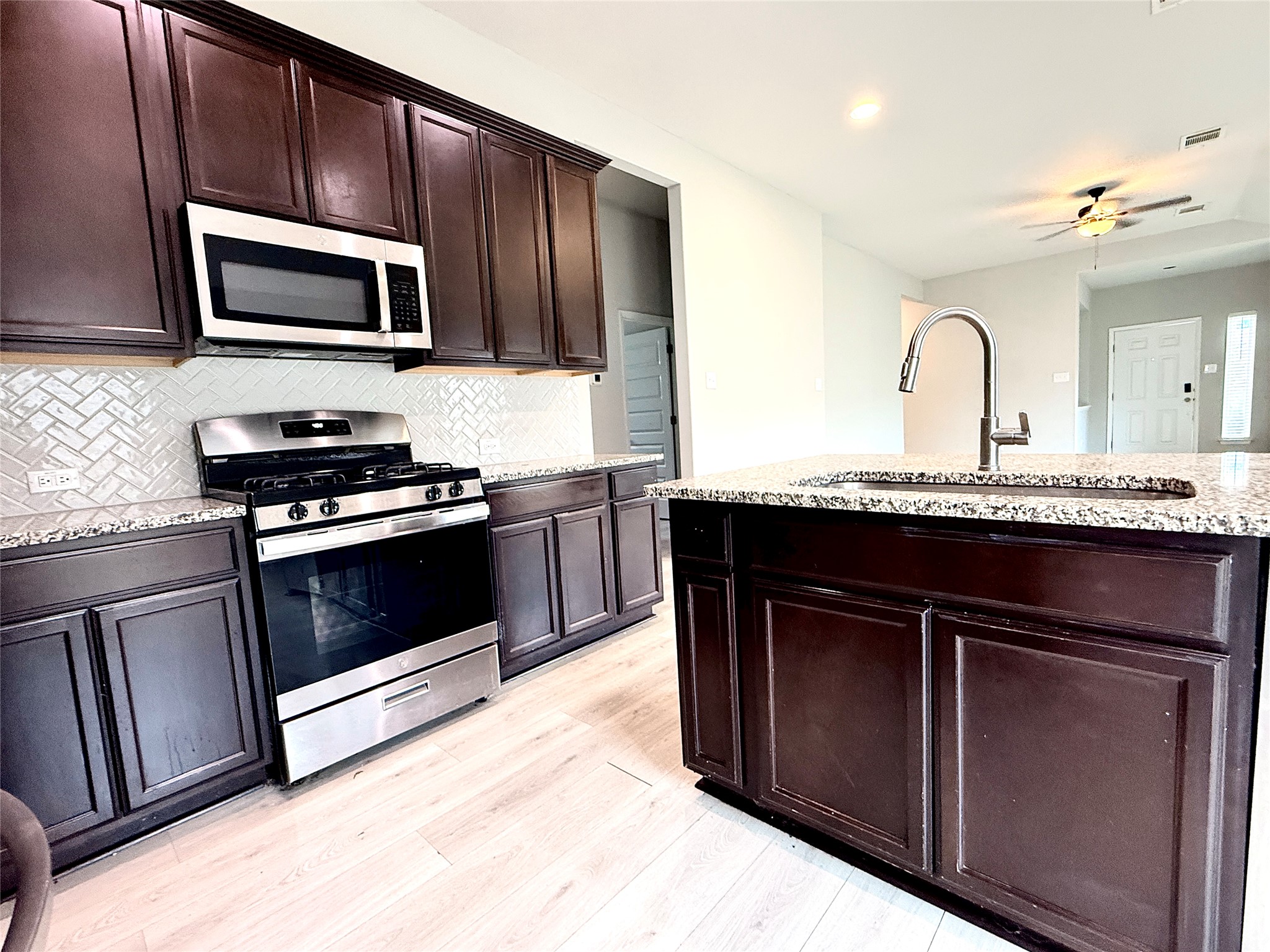 5629 Corso Court Austin, TX 78747 - Photo 8 of 23 Kitchen with stainless steel appliances, dark wood finish cabinetry, ceiling fan, light stone countertops, and light wood-style floors