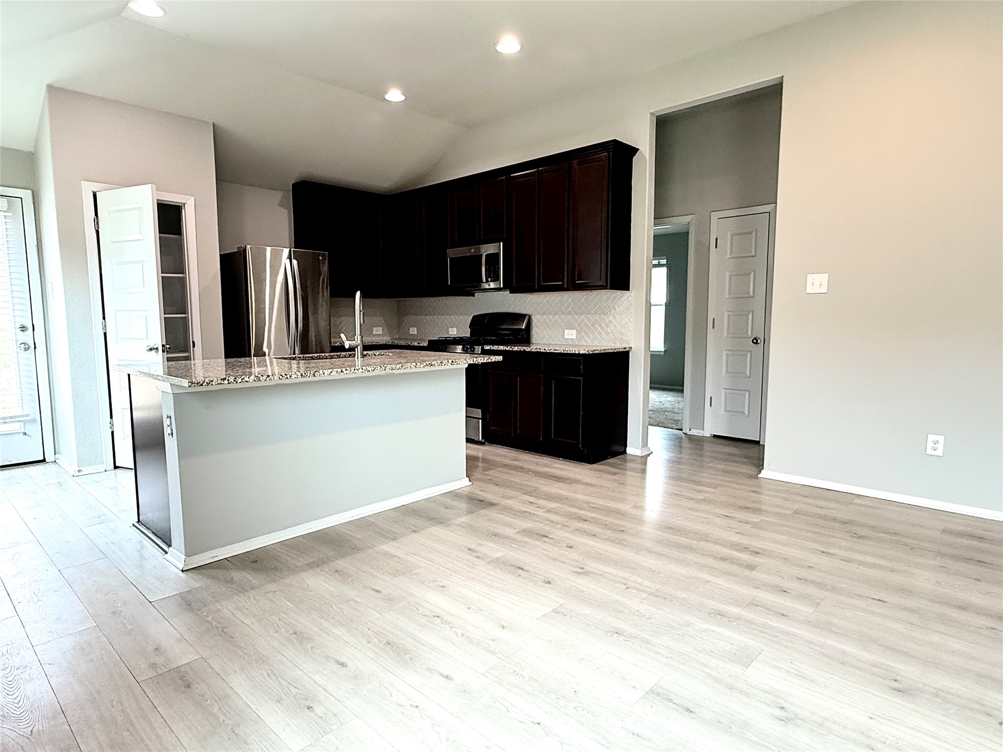 5629 Corso Court Austin, TX 78747 - Photo 10 of 23 Kitchen with stainless steel appliances, a center island with sink, light wood finished floors, light stone counters, and vaulted ceiling
