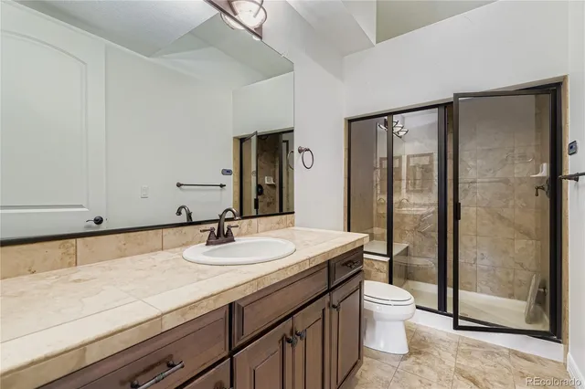 a bathroom with a granite countertop sink a toilet a mirror and shower