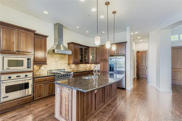 a kitchen with kitchen island granite countertop a stove a sink a refrigerator and a wooden floor