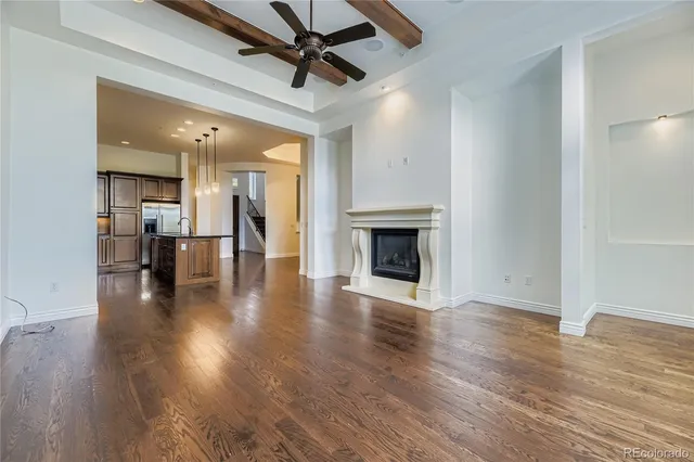 an empty room with wooden floor fireplace and a kitchen view