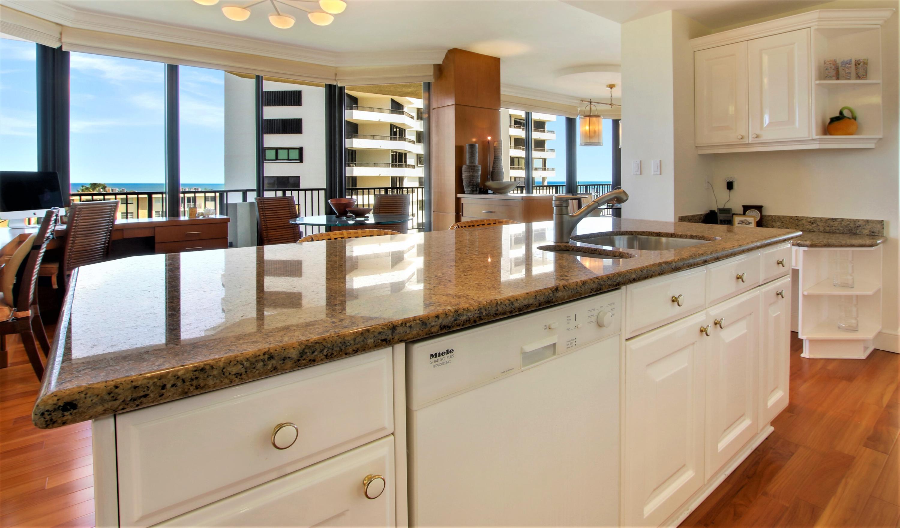 570 Ocean Drive, Unit 601 Juno Beach, FL 33408 - Photo 11 of 35 a large white kitchen with granite countertop a sink and white cabinets next to a large window
