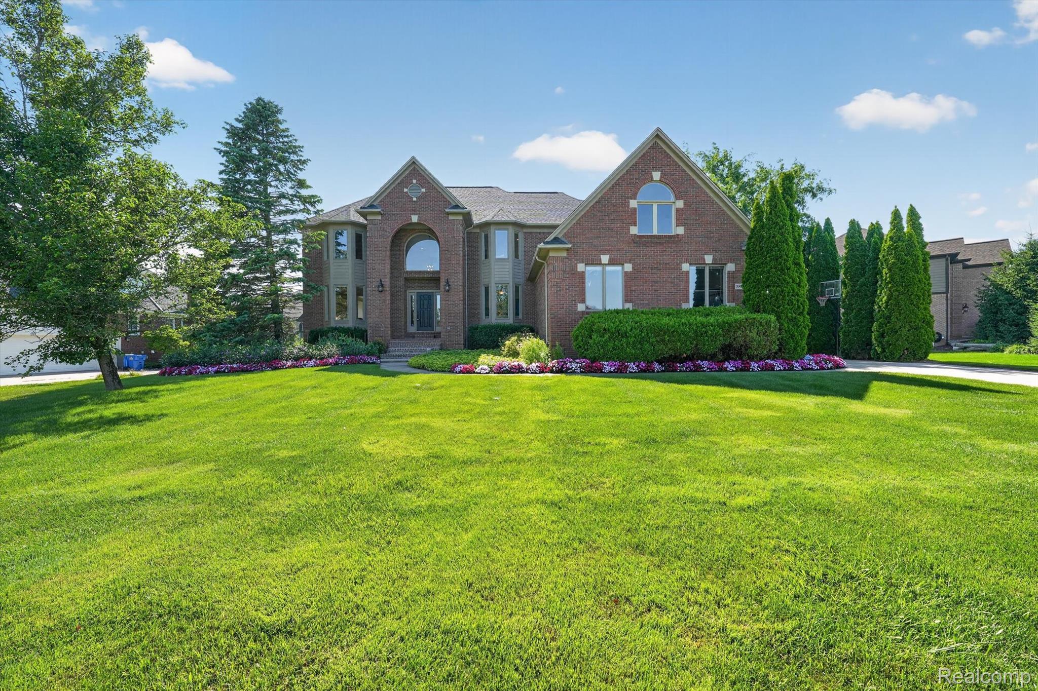 Brick-clad residence featuring a symmetrical facade, an arched entryway, multiple gabled rooflines, and a verdant front lawn with mature landscaping
