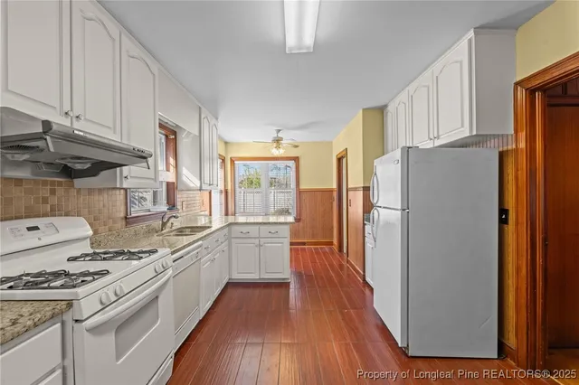 a kitchen with stainless steel appliances a refrigerator a stove a sink and white cabinets with wooden floor