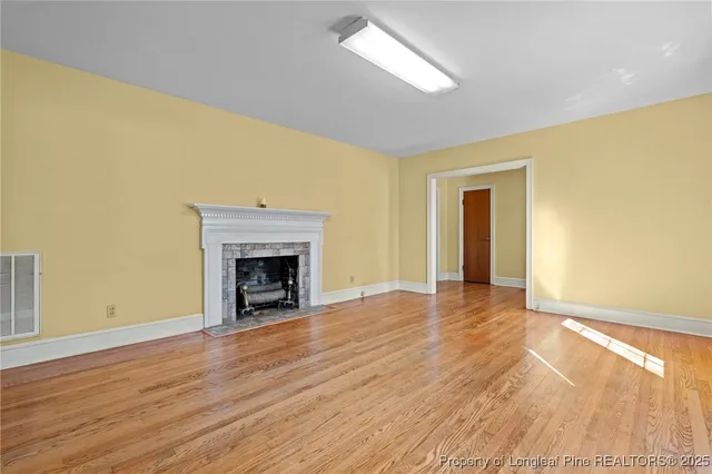 a view of an empty room with wooden floor and a fireplace