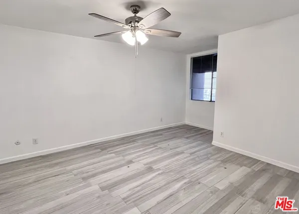 an empty room with wooden floor fan and windows