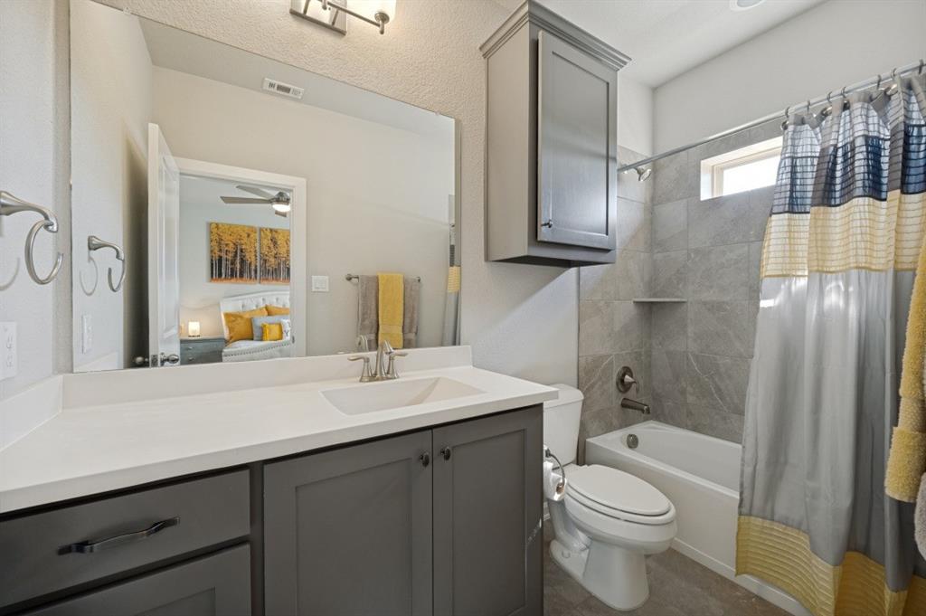 2721 Old Shire Path Road Prosper, TX 75078 - Photo 24 of 39 Bathroom featuring a vanity with a white countertop and gray cabinetry, a rectangular undermount sink, a large wall-mounted mirror, a tub/shower combination with gray tile surround, and a wall-mounted gray cabinet