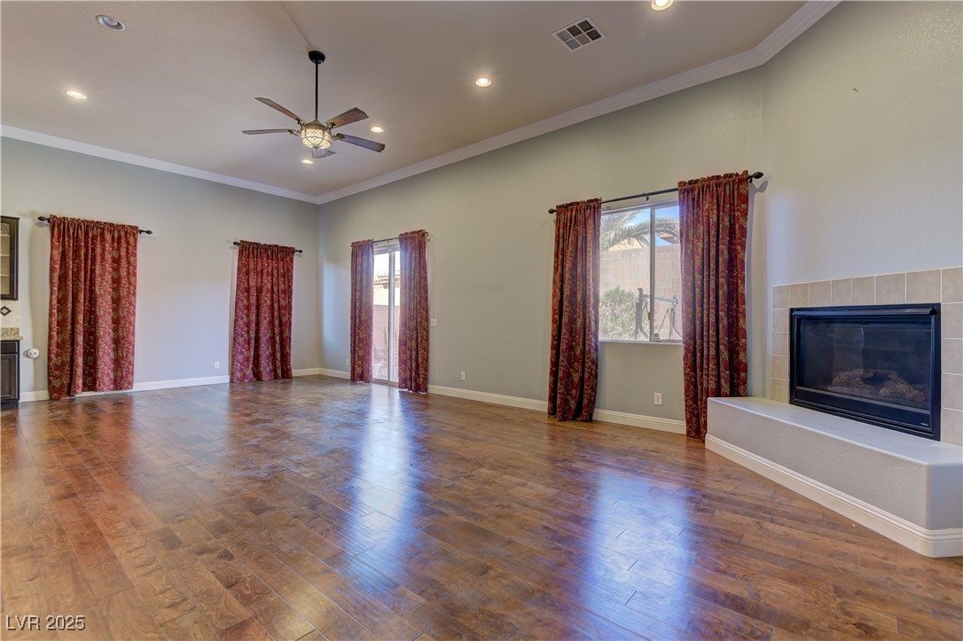 972 Rue Grand Paradis Lane Henderson, NV 89011 - Photo 11 of 32 Unfurnished living room featuring a tile fireplace, crown molding, hardwood / wood-style floors, a ceiling fan, and plenty of natural light