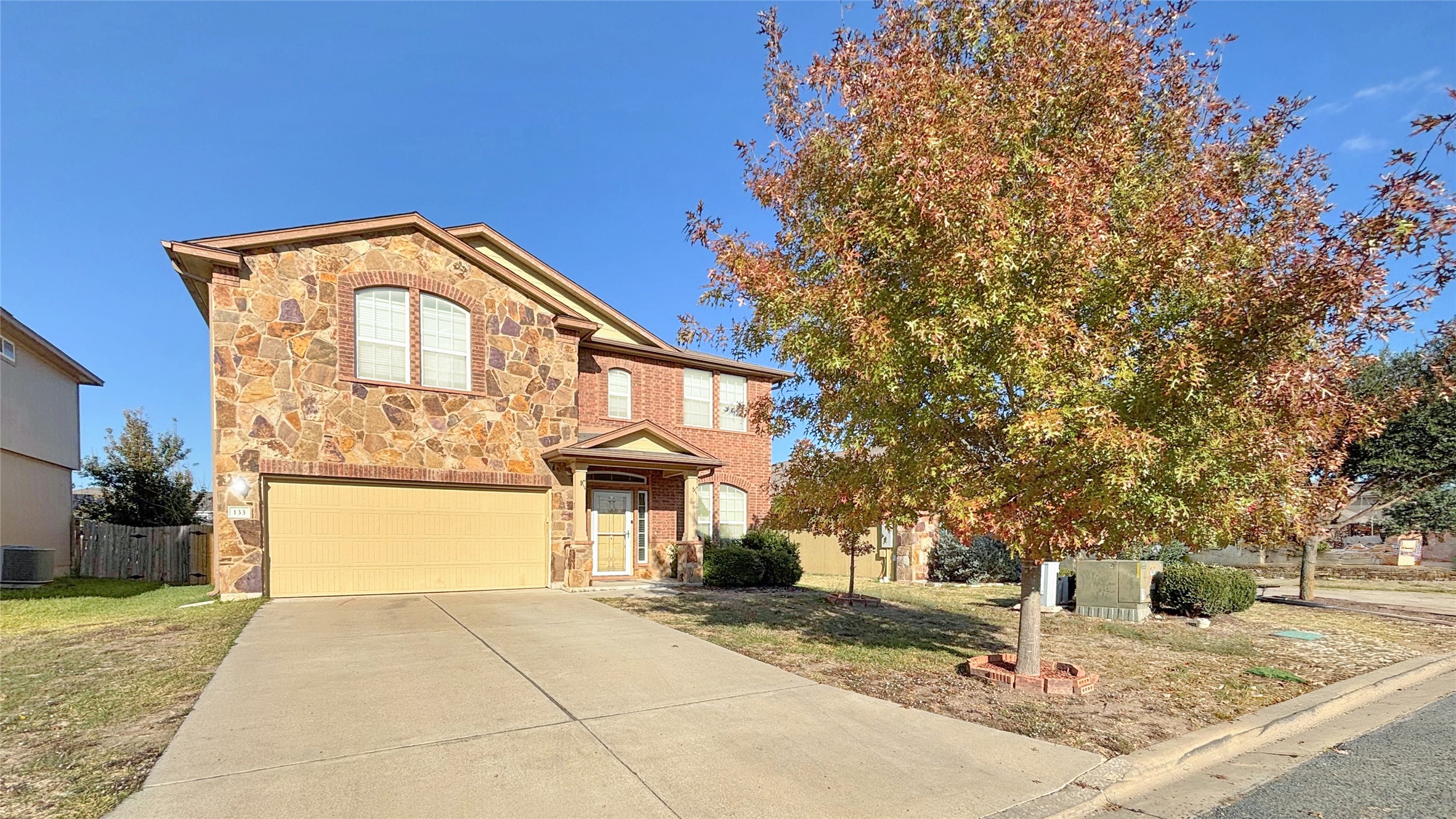 133 Langtry Lane Jarrell, TX 76537 - Photo 19 of 28 Traditional-style house featuring stone siding, an attached garage, sprinkler system, gutters, and driveway.