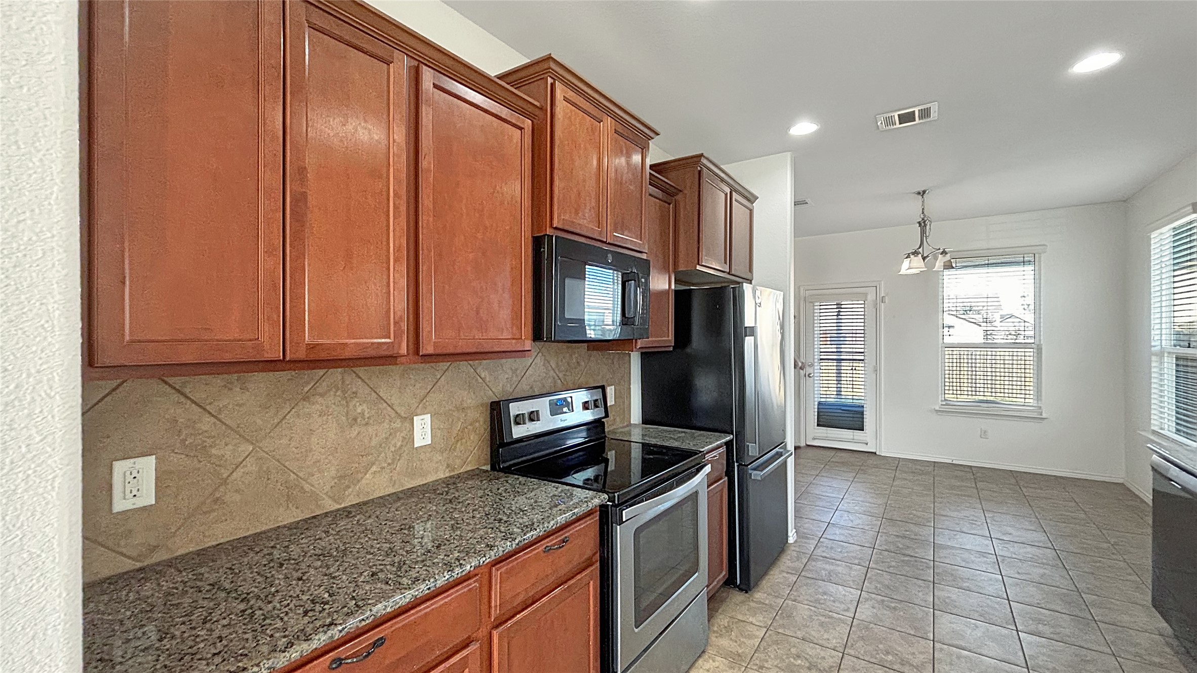 133 Langtry Lane Jarrell, TX 76537 - Photo 6 of 28 Spacious Kitchen conveniently located just off of the living room with stainless steel electric range, granite counters, microwave, and brown cabinetry.