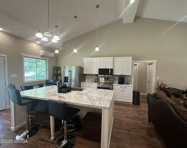 a kitchen with stainless steel appliances kitchen island granite countertop a dining table chairs and refrigerator