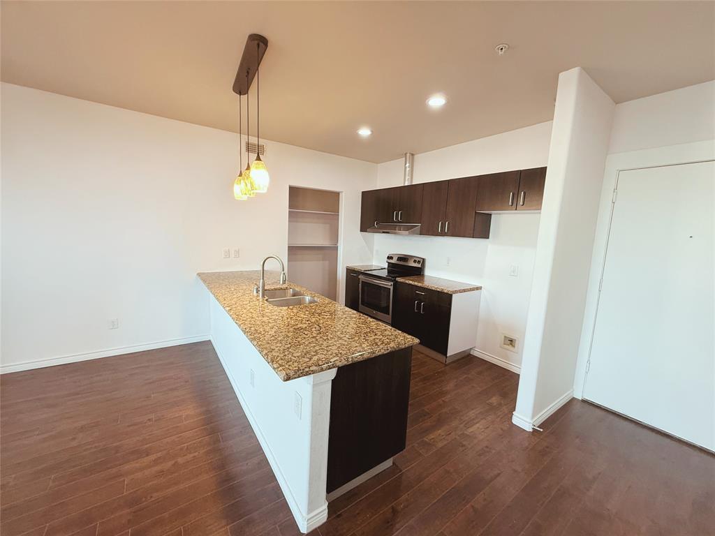 1100 West Trinity Mills Road, Unit 4042 Carrollton, TX 75006 - Photo 9 of 19 Kitchen featuring stainless steel range with electric cooktop, a peninsula, dark brown cabinets, dark wood-style flooring, and light stone countertops
